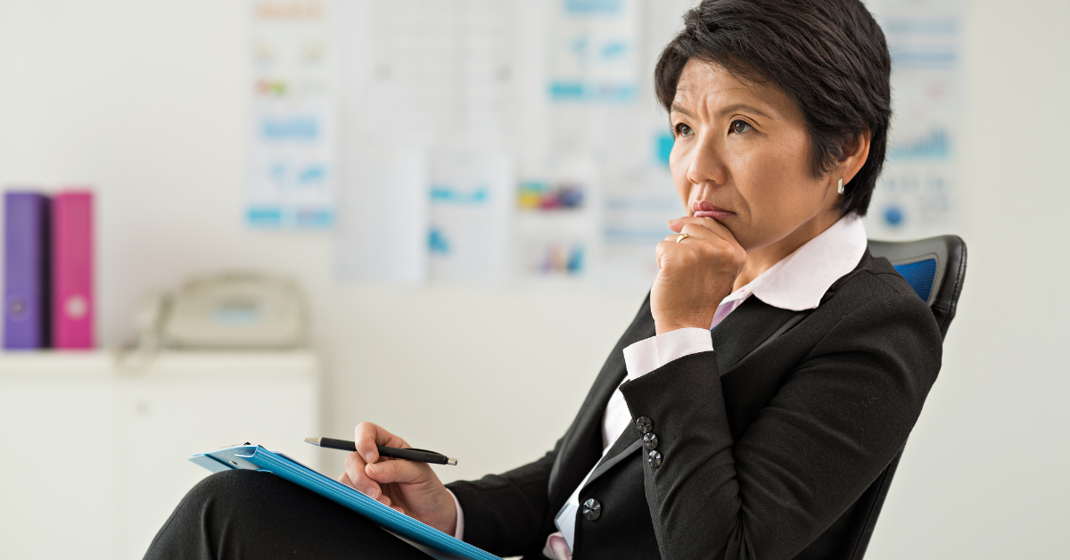 Woman with concerned look sitting in desk chair with notebook and pen