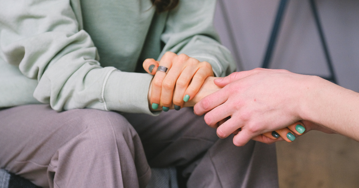 Two people holding hands in a comforting gesture in a certified community behavioral health clinics setting.