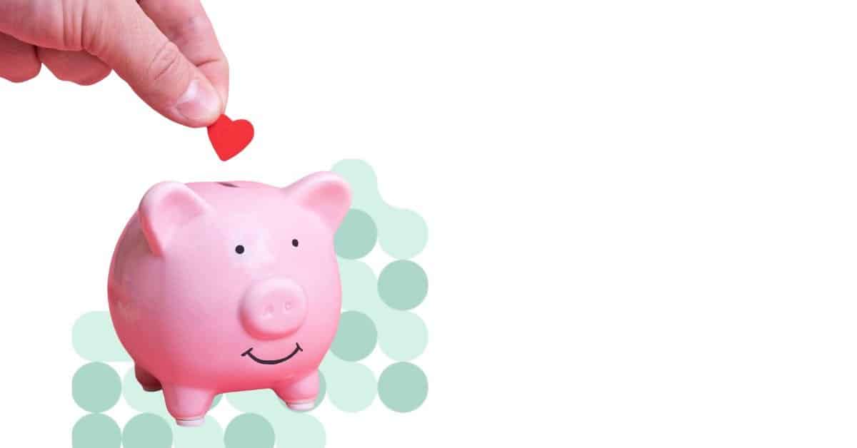 A hand is putting a red heart into a pink piggy bank representing braided funding.